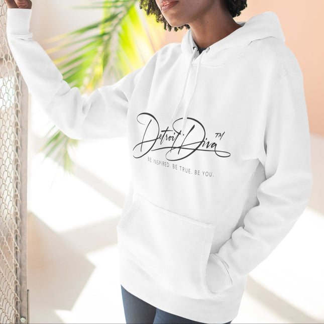 Person wearing a white hoodie with 'Detroit Diva' text, standing against a blurred outdoor background.