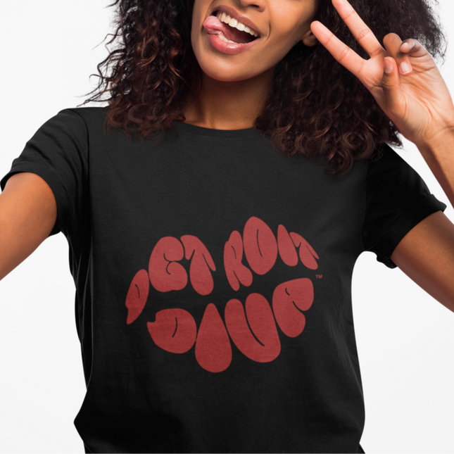 Person wearing a black t-shirt with red text, that says Detroit Diva shaped like lips making a peace sign.