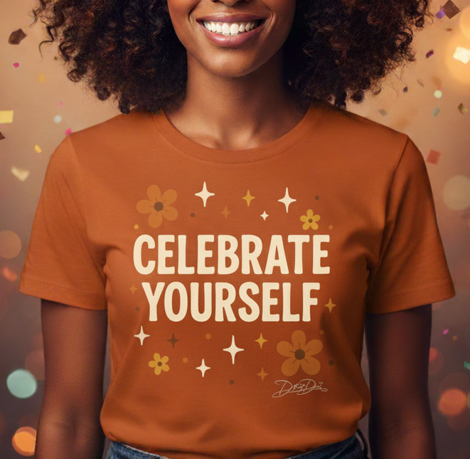 Woman wearing a 'Celebrate Yourself' t-shirt against a festive background with colorful lights.
