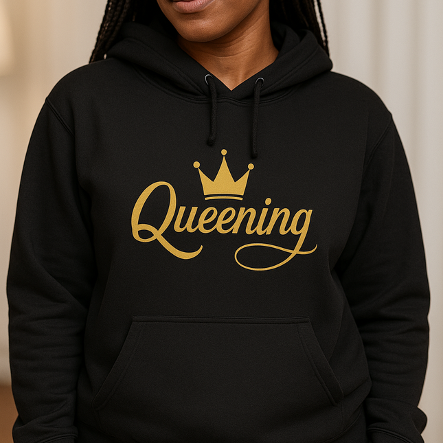 Person wearing a black hoodie with 'Queening' printed in gold on a beige background