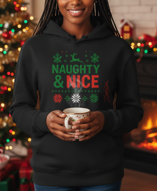 Woman wearing a 'Naughty & Nice' hoodie holding a mug in a festive room with Christmas decorations.