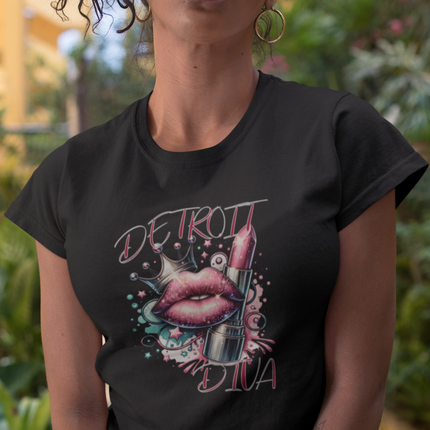 Person wearing a black t-shirt with 'Detroit Diva' design with lips, lipstick, and glitter sitting outdoors.