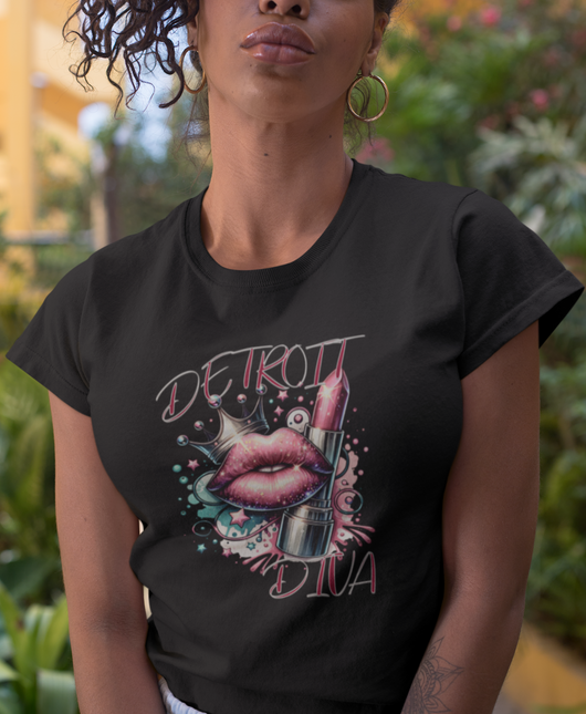 Person wearing a black t-shirt with 'Detroit Diva' design with lips, lipstick, and glitter sitting outdoors.
